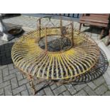 A painted wrought metal two-piece circular garden bench with strap work seat, dia. 140cmRusty and