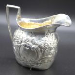 A late Victorian silver cream jug of helmet shape having a repoussee scrolling and floral