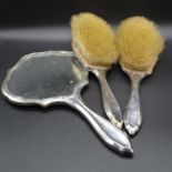 An early 20th century silver backed hand mirror together with two matching silver backed brushes (
