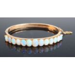 A rose metal opal oval hinged bangle, with box clasp and safety chain, featuring 13 graduated oval