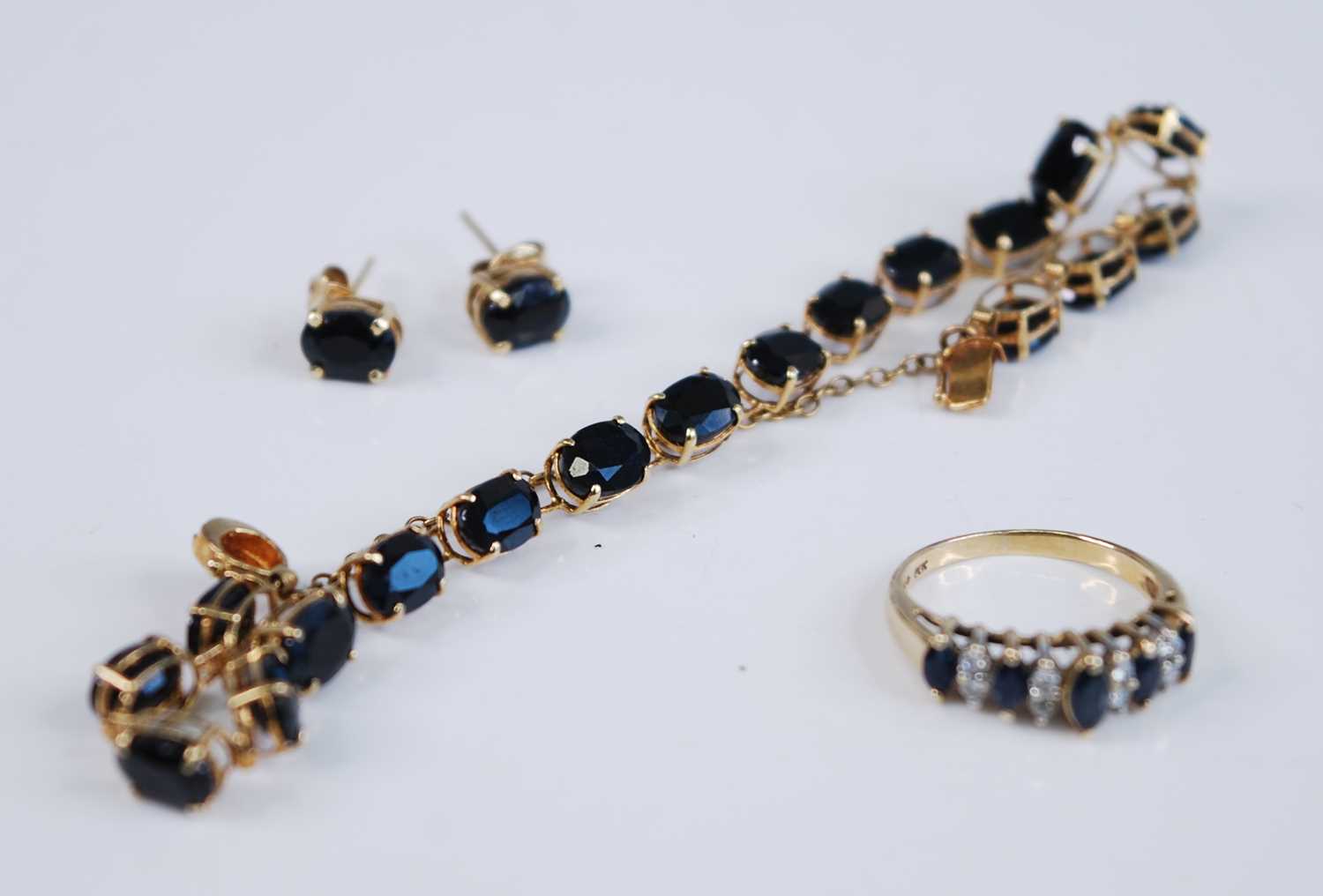 A yellow metal sapphire suite, comprising a sapphire line bracelet featuring 18 oval faceted