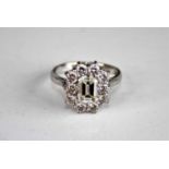 A white metal diamond rectangular cluster ring, featuring a centre emerald cut diamond within a