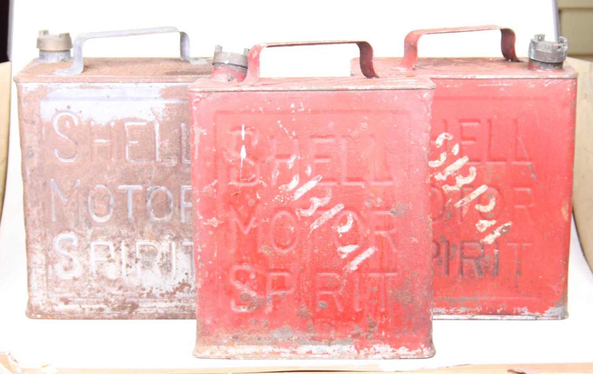 A pair of Shell red pained metal fuel cans, together with one other grey painted example (3)