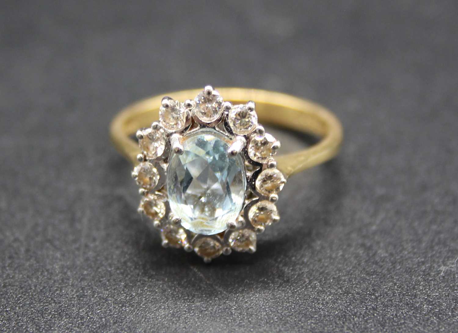 An 18ct gold, aquamarine and diamond flower head cluster ring, the oval cut aquamarine measuring