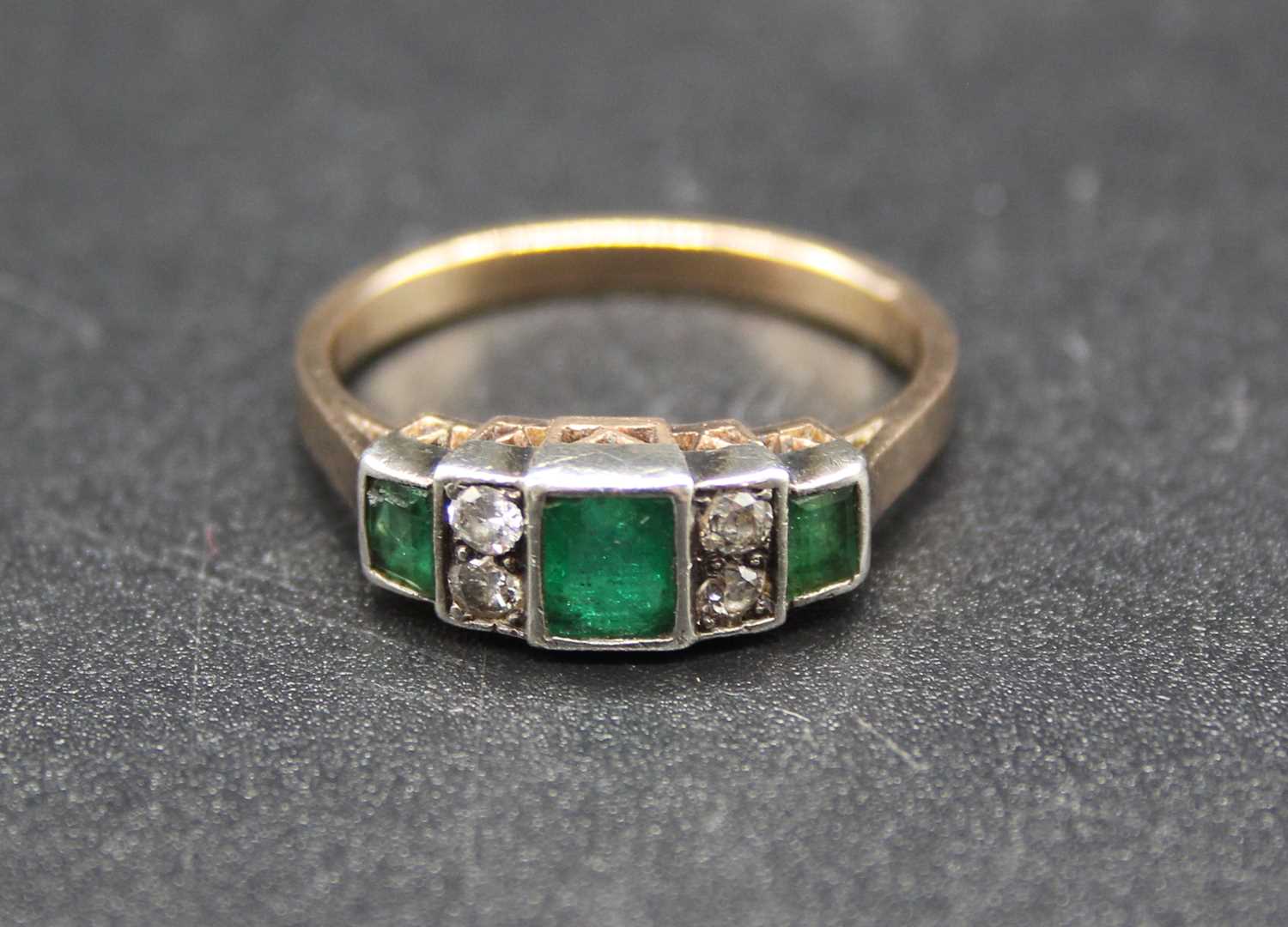 An Art Deco yellow metal, emerald and diamond dress ring, arranged as a centre emerald cut emerald