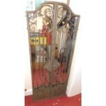 A French "aged" wrought metal twin shuttered door mirror, of arch and scroll floral decorated