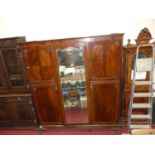 An early 20th century mahogany triple wardrobe, having central bevelled mirror door on acanthus leaf