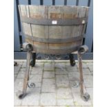A coopered oak cylindrical log bucket raised on black painted wrought iron scroll decorated stand,