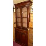 A mid Victorian mahogany round cornered bookcase cupboard, having twin arched glazed upper doors