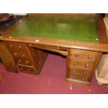 An early 20th century oak and green leather inset kneehole writing desk, having an arrangement of