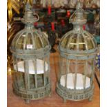 A pair of painted metal and glazed lanterns, each surmounted by a spring handle, standing on