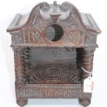 An early 20th century carved oak pocket watch holder of architectural form, having a swan neck