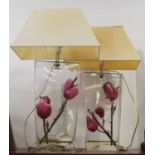 A pair of contemporary table lamps, each in the form of purple flowers within a shaped glass case,