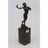 A reproduction bronzed figure of nude boy in standing pose with slingshot in hand, on a naturalistic