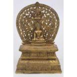 A reproduction bronze alloy shrine in the form of a deity in seated lotus pose against a pierced