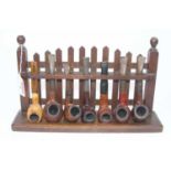 An early 20th century oak pipe rack in the form of a picket fence, containing various pipes to