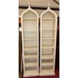 A pair of contemporary painted and narrow freestanding open display shelves, having arched finialled