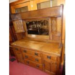 An Arts & Crafts oak mirror back sideboard having opposing upper credence doors over base fitted