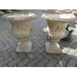 A pair of reconstituted stone pedestal garden urn planters, each in the classical taste, decorated