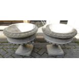 A pair of reconstituted stone squat footed circular pedestal urn planters in the classical taste,