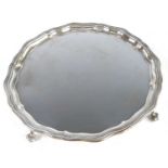 A George V silver salver, of shaped circular form having a stepped wavy rim, standing upon four claw