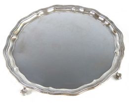 A George V silver salver, of shaped circular form having a stepped wavy rim, standing upon four claw