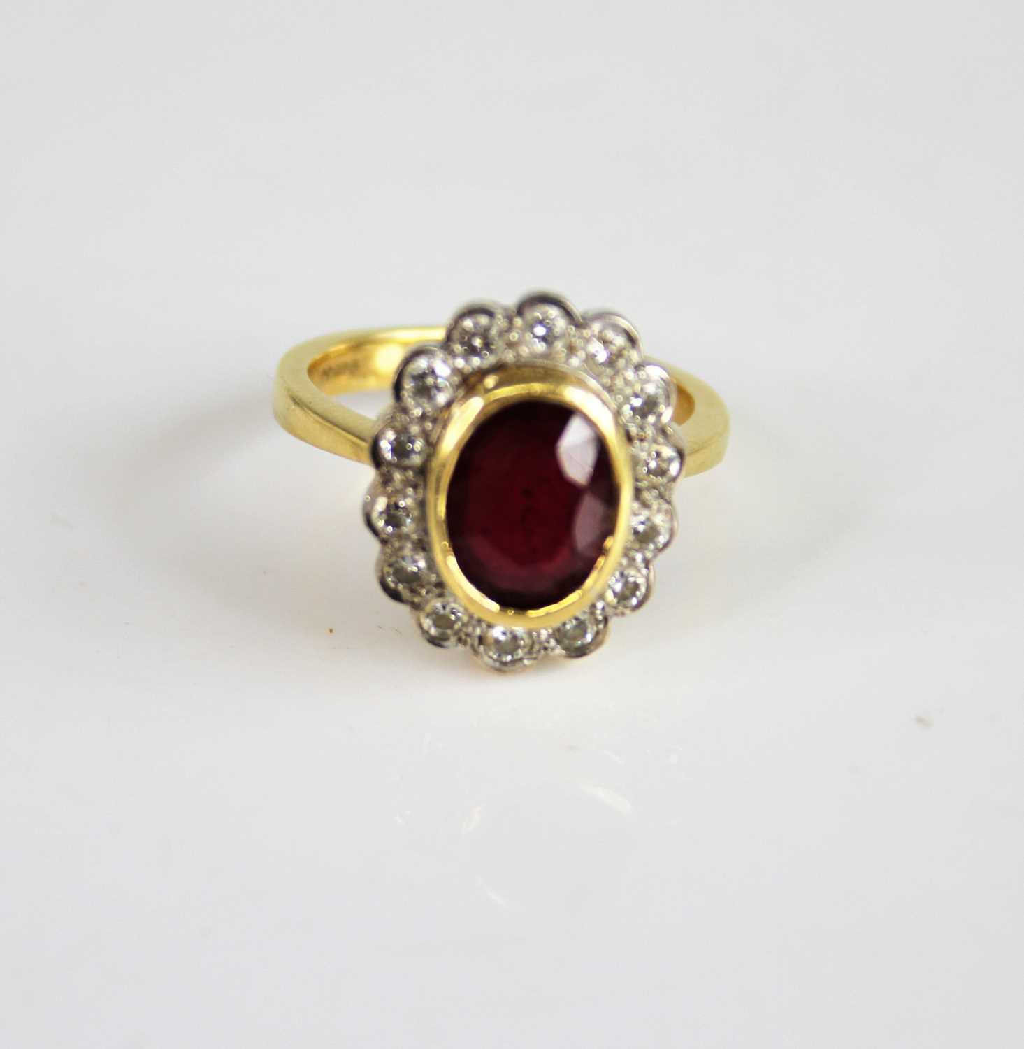 An 18ct yellow and white gold ruby and diamond oval cluster ring, featuring a centre oval facetted