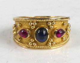 A yellow metal Etruscan style dress ring, having a centre oval synthetic sapphire and two
