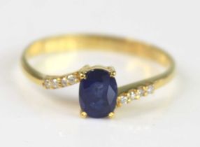 A yellow metal sapphire and diamond crossover style dress ring, having a centre oval sapphire and