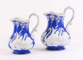 A graduated set of two Victorian relief moulded pottery jugs, each decorated with swans, largest