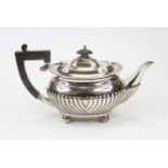 A George V silver teapot, of half-fluted bombe form, having ebonised finial and handle, on ball