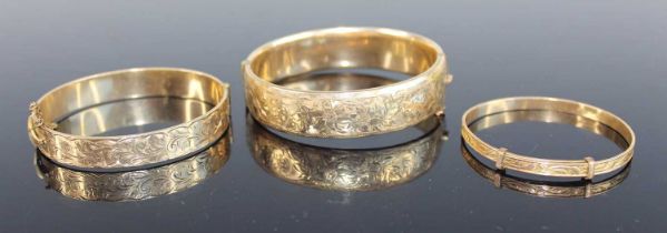 A Victorian style rolled gold hinged bangle, having flower engraved decoration and safety chain,