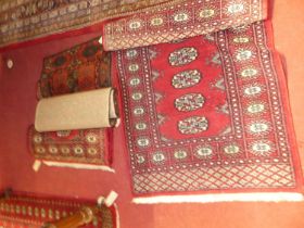 Three small Persian woollen red ground Bokhara rugs, together with one other machine woven similar