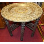 A Benares brass topped occasional table, on carved hardwood folding base.