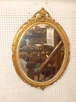 A giltwood and gesso oval wall mirror, having a floral decorated surmount, 73.5 x 53cm