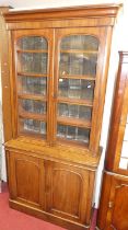 A Victorian mahogany round cornered bookcase cupboard, having twin arched glazed upper doors,