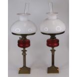 A pair of Victorian brass oil lamps, each having a milk glass shade and cranberry glass font, h.57cm