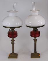 A pair of Victorian brass oil lamps, each having a milk glass shade and cranberry glass font, h.57cm