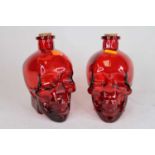 A pair of cranberry glass decanters in the form of skulls, h.17cm