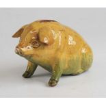 An Ewenny pottery piggy bank, shown in seated pose, having a mottled yellow and green glaze and