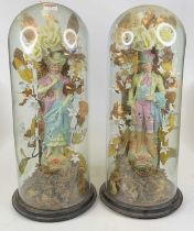 A pair of bisque porcelain figures, each shown in 18th century dress, each housed beneath a glass