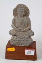 An Indian clay Buddha amulet, Gandharan form, mounted on a hardwood plinth, h.19cm