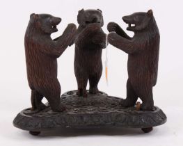 An early 20th century Black Forest carved wood model of three standing bears, on shaped conforming