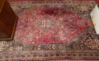 An Iranian red ground woollen Shiraz rug, having a lozenge ground within trailing tramline