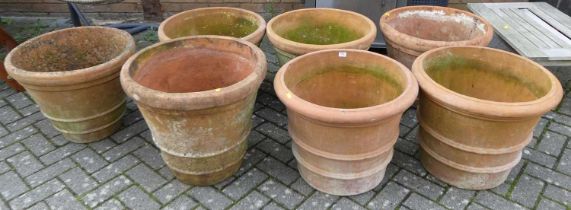 A collection of seven similar large terracotta cylindrical tapering planters, each diameter approx