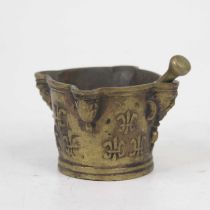 A bronze pestle and mortar, the mortar having proud mask corners with applied fleur de lys motifs,