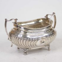 A George III silver sugar bowl, of half-gadrooned bombe form, with shaped twin handles, on cast