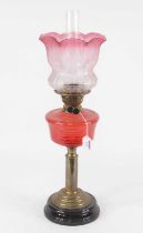 An early 20th century oil lamp, having an associated cranberry tinted etched glass shade above a red