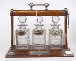 An Edwardian oak three bottle tantalus having silver plated mounts, containing three cut glass