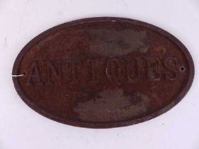 A cast iron sign of oval shape, titled 'Antiques', 21 x 34cm